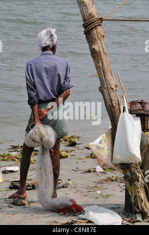 Vista posteriore del pescatore indiano che tiene la rete di casting della spiaggia presa sulle rive dell'estuario a Fort Cochin, Kochi, Kerala, India Foto Stock