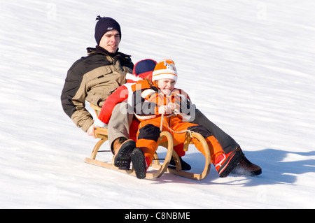 Padre con le sue figlie slittino sulla neve giù per la collina. Foto Stock