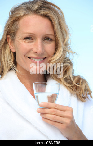 Donna di bere un bicchiere di acqua in un accappatoio Foto Stock
