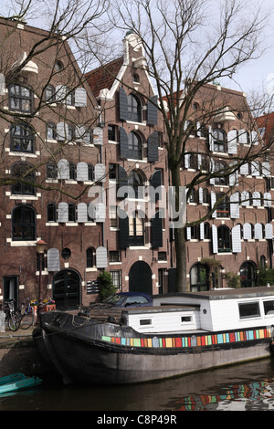 Casa galleggiante olandese barge e vecchi magazzini case su un canale nel quartiere Jordaan di Amsterdam Holland Olanda in primavera Foto Stock