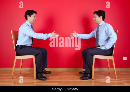 Accordo di stretta di mano tra due letti imprenditore seduto in una sedia accanto ad una parete rossa Foto Stock