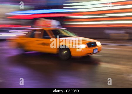 Un giallo taxi è una sfocatura come si precipita attraverso le luci di Times Square di notte a New York City. Foto Stock