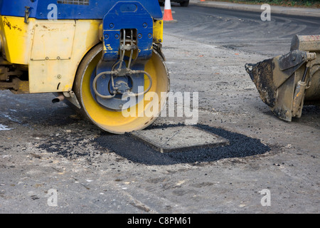 Uso del rullo di strada di asfalto compatto attorno ad un tombino prima strada è spianata. Foto Stock