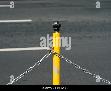 Una sottile barriera giallo pole e due catene collegate ad esso contro un asfalto grigio dell'autostrada. Foto Stock