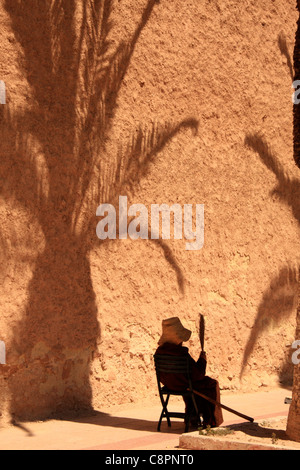 Signora anziana ventole se stessa nell'ombra di una palma da mura che circondano la medina di Essaouira, Marocco, Africa Foto Stock