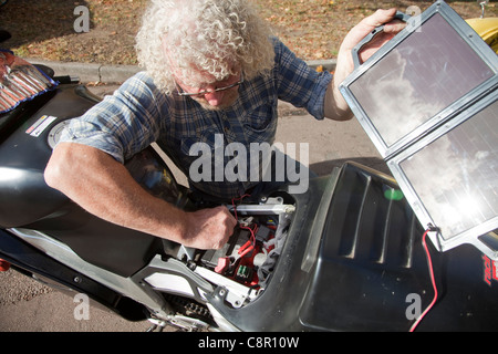 Un uomo le tasse il suo moto batteria con un caricabatterie solare REGNO UNITO Foto Stock