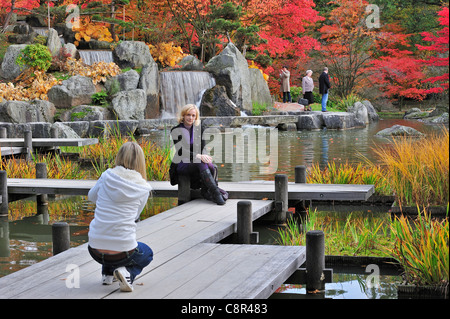 Tourist in posa per la telecamera sulla passerella di legno nel giardino giapponese con chioma in rosso i colori autunnali in Hasselt, Belgio Foto Stock