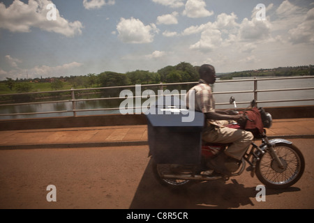 Un motociclista trasporta una bara attraverso il fiume Nilo in Jinja, Uganda. Foto Stock