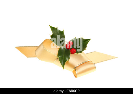 Decorazione di Natale un nastro color oro di prua e holly rametto con bacche rosse isolata contro bianco Foto Stock