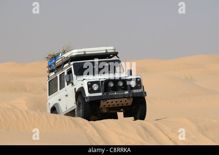 Africa, Tunisia, nr. Tembaine. Land Rover Defender 110 TD5 Station Wagon sulla sua strada attraverso un tratto di dune di sabbia vicino al ... Foto Stock