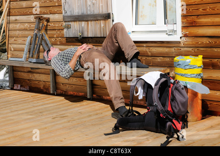 Un uomo addormentato al sole su una panca in legno Foto Stock