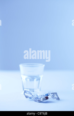 Confezione blister con una capsula con un bicchiere di acqua in background Foto Stock