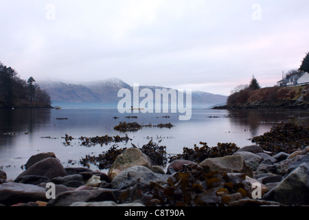 Scottish loch presa lungo la riva con montagne innevate in lontananza. Foto Stock