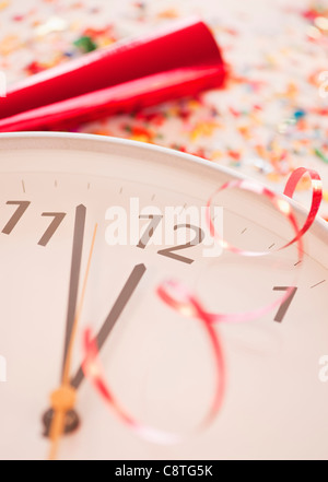 Coriandoli e nastri su orologio che mostra cinque minuti a mezzanotte Foto Stock