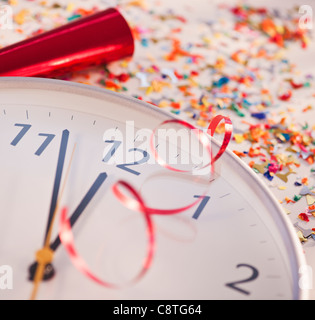 Coriandoli e nastri su orologio che mostra cinque minuti a mezzanotte Foto Stock