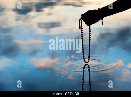 Mano azienda Rudraksha indiano / Japa Mala i grani di preghiera su acqua increspata . Silhouette Foto Stock