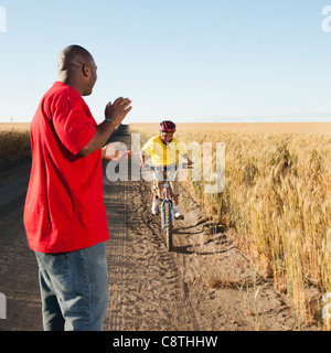 Stati Uniti d'America, Oregon, Wasco, Padre battendo le mani come figlio è escursioni in bicicletta lungo la strada sterrata nei campi Foto Stock