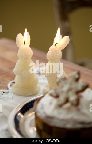 Forma di coniglio candela accesa e una fetta di torta sulla scrivania Foto Stock