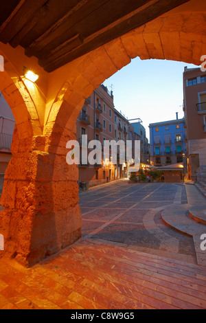 Vista della piazza Santiago Rossinyol attraverso un arco del XIV secolo in via Merceria illuminata al crepuscolo nella città vecchia di Tarragona, Catalogna, Spagna Foto Stock