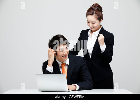 Asian imprenditrice Guardando imprenditore seduto alla scrivania con computer portatile Foto Stock