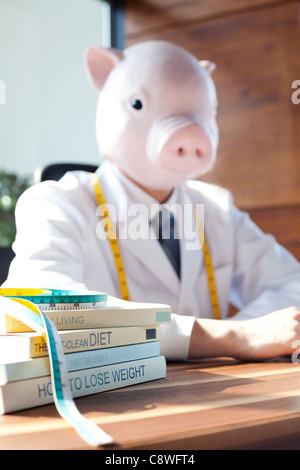 Testa di maiale nutrizionista con la dieta Libri e nastro di misurazione sulla scrivania Foto Stock