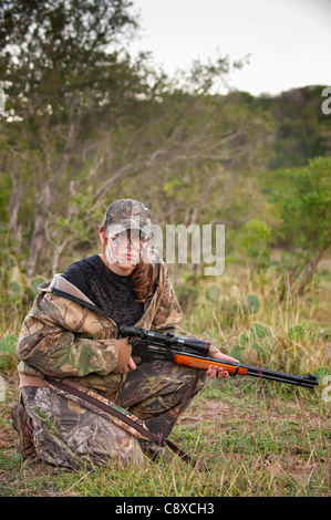 L'immagine verticale del cacciatore femmina con un fucile in camuffamento vestito e faccia Foto Stock