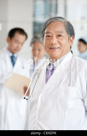 Senior medico con medici e infermiere in background Foto Stock