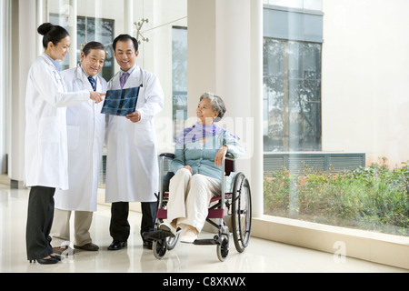 Senior donna attende in una sedia a rotelle mentre i medici discutere la sua scansione a raggi X Foto Stock