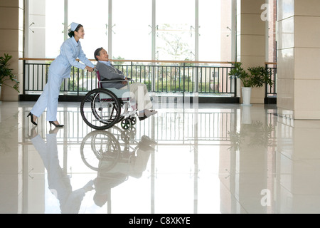 Infermiere Senior spinge l'uomo in una sedia a rotelle Foto Stock