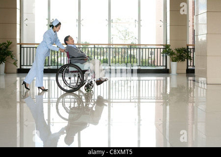 Infermiere Senior spinge l'uomo in una sedia a rotelle Foto Stock