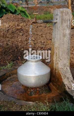 Acqua potabile a cascata da un tubo di supporto e cadere in una pentola in alluminio su una riva di un fiume in Backwaters nel Kerala, India Foto Stock