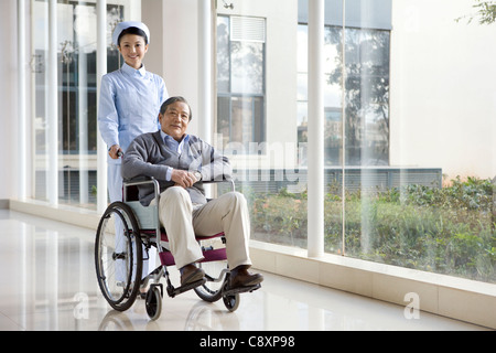 Infermiere Senior spinge l'uomo in una sedia a rotelle Foto Stock