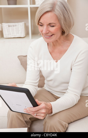 Attraente senior eleganti donna che utilizza un computer tablet a casa. Foto Stock