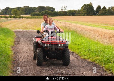 Un giovane ragazzo ha una corsa su di una moto quad con un adulto sul retro su una farm Regno Unito Foto Stock