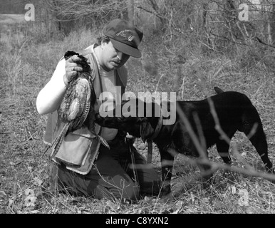 Foto in bianco e nero di hunter tenendo premuto fino al fagiano con Labrador Retriever cerca su Foto Stock