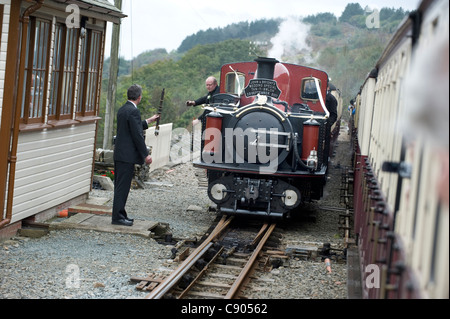 Il driver del motore di 2ft. A scartamento ridotto locomotiva a vapore double Fairlie "Conte di Merioneth' si prepara per scambiare la singola linea gettoni con il segnalatore a Tan -Y - stazione di Bwlch sulla ferrovia Ffestiniog Foto Stock