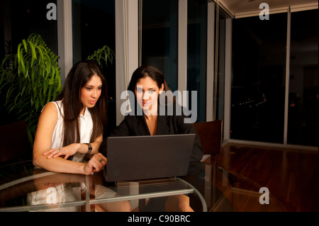Due giovani donne ispaniche sorelle 20s-30 il lavoro a casa in appartamento urbano di notte sul computer portatile Foto Stock