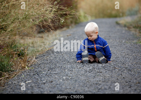 Tre anni di vecchio ragazzo seduto sul percorso, capelli biondi, blue coat. Foto Stock