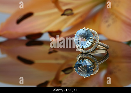 Anello d'oro con una grande gemma sulla superficie di mirroring e un grande giglio rosso su uno sfondo Foto Stock