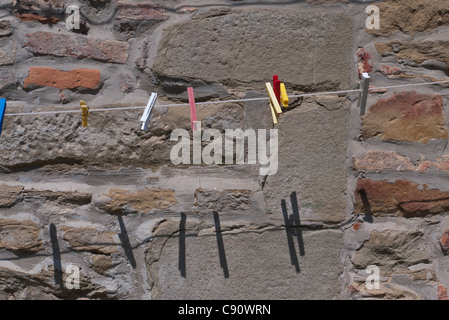 Colorate perni di vestiti appesi ad un linea di abbigliamento contro un muro di pietra sfondo nella città italiana di Panicale. Foto Stock