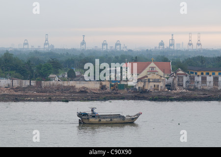 Vecchia vela chiatta giù il fiume SAIGON in Ho Chi Minh City, Vietnam con il moderno porto di gru in background. Foto Stock