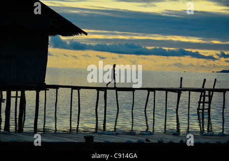 Lone donna camminando sul molo, tramonto, mare, Kri Eco Resort Raja Ampat isole della Papua occidentale nell'Oceano Pacifico, Indonesia. Foto Stock