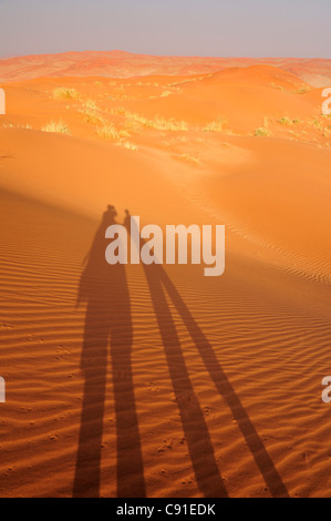 Due persone che si tengono per mano di gettare ombra sulle dune di sabbia rossa, Namib Rand Riserva Naturale, Namib Desert, Namib, Namibia Foto Stock