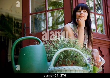 Donna seduta con piante sulla veranda sul retro Foto Stock