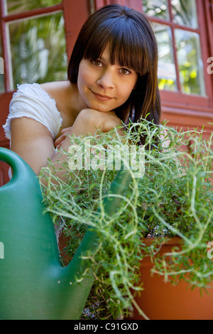 Donna seduta con piante sulla veranda sul retro Foto Stock