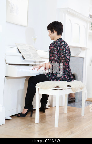 Donna suonare il pianoforte a casa Foto Stock