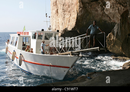 Imbarcazione turistica cercando di tie-up per consentire ai turisti di sbarcare al livello del mare ingresso alla Grotta di Nettuno Grotta di Nettuno su Foto Stock