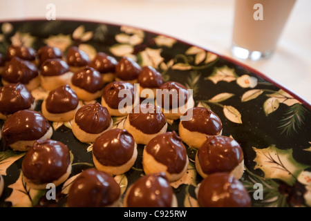 Primo piano di un raffinato nero e oro vassoio di ciliegia-riempito i cookie, mano-immersi nel cioccolato per Natale con un bicchiere di latte Foto Stock