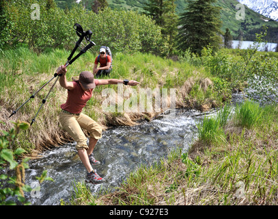 Escursionista femmina salta un torrente lungo Crescent Lake mentre backpacking in Chugach National Forest, Penisola di Kenai, Alaska Foto Stock