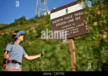 La donna legge chilometraggio percorso firmare mentre escursionismo il North Face Trail presso Alyeska Resort in Girdwood centromeridionale, Alaska, estate Foto Stock